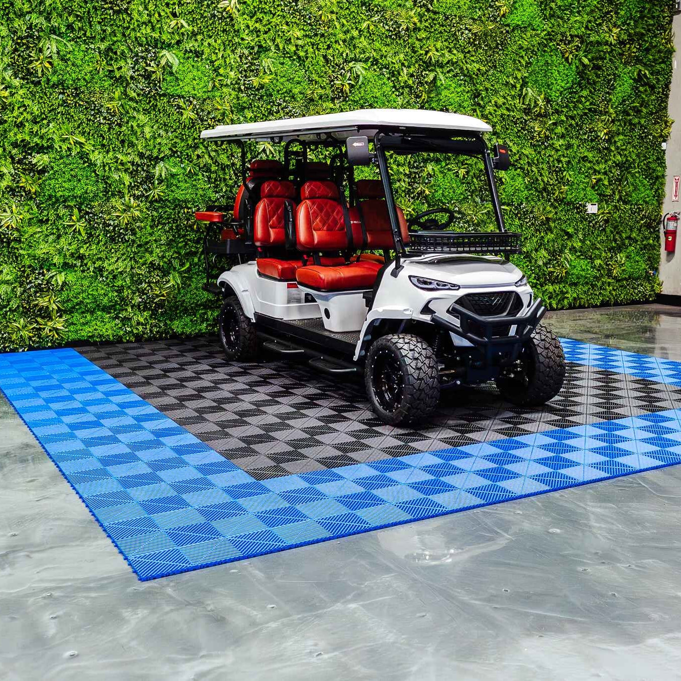White golf cart with red seats on a blue checkered mat in front of a green wall.