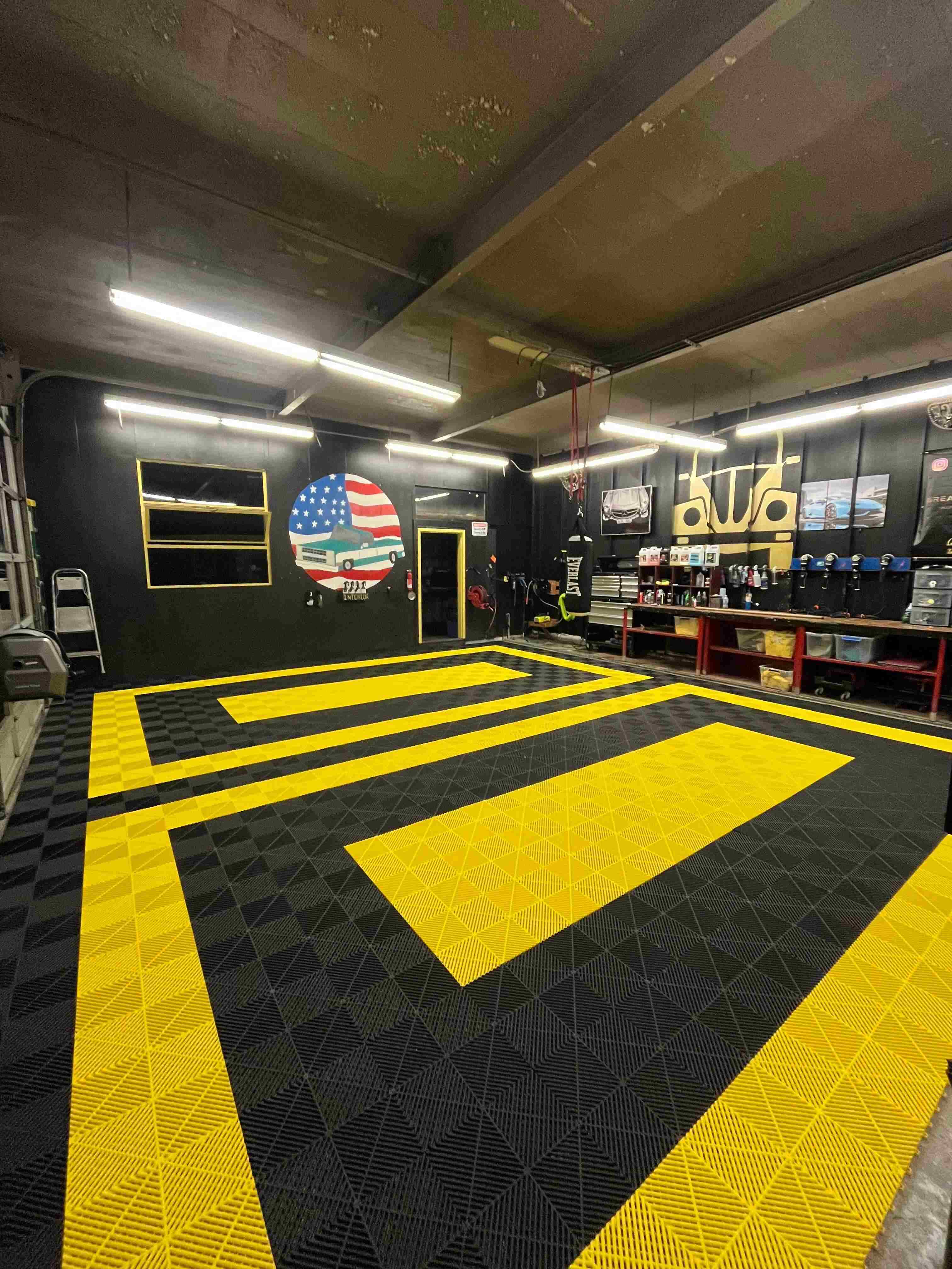 Garage interior with black and yellow floor design, American flag logo on wall, and various equipment.
